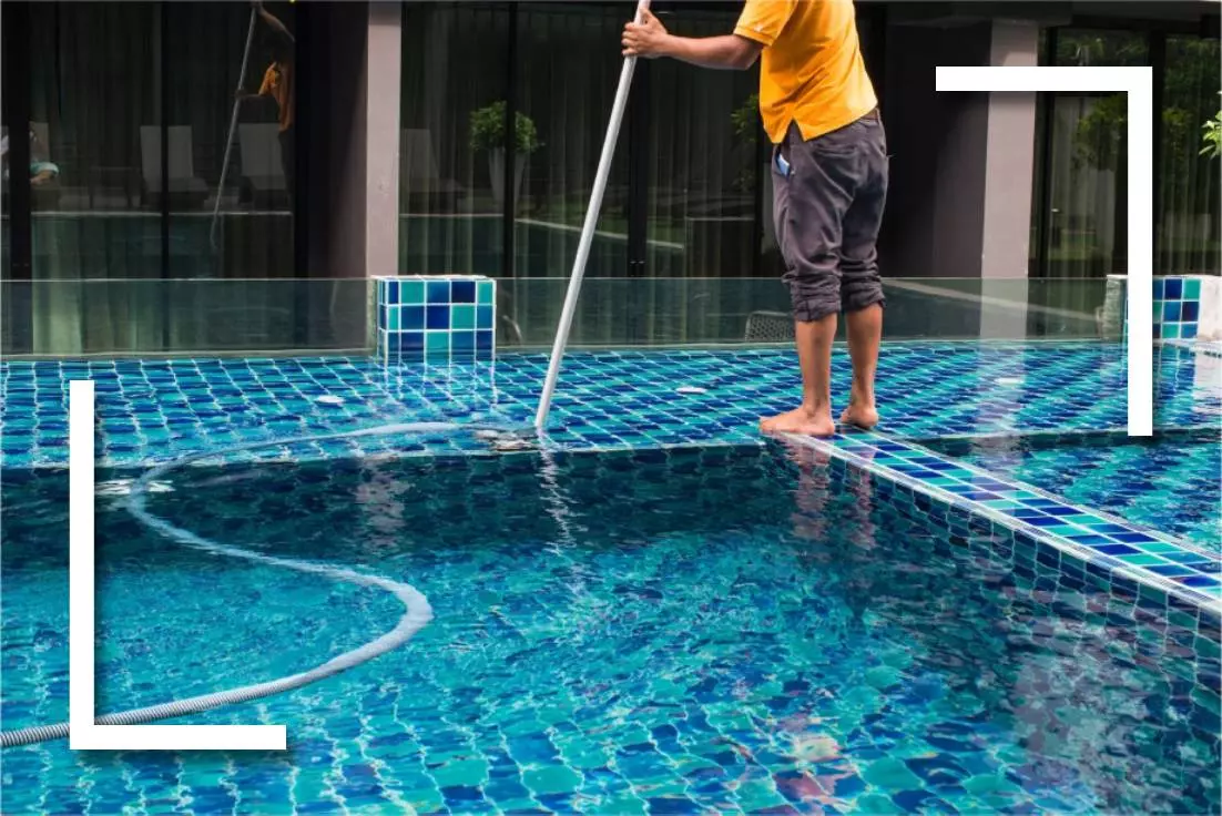 A man cleaning the pool with a mop.